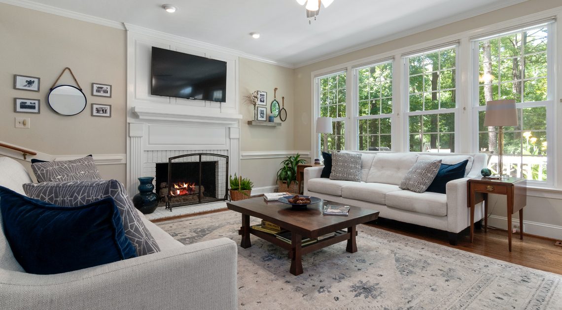 A modern living room features a flat-screen TV, a modern white couch, a coffee table, pictures on the wall, a ceiling fan, and lamps.